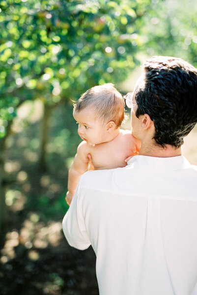 Man holds a baby in his arms while standing in the garden. Back view Stock Image