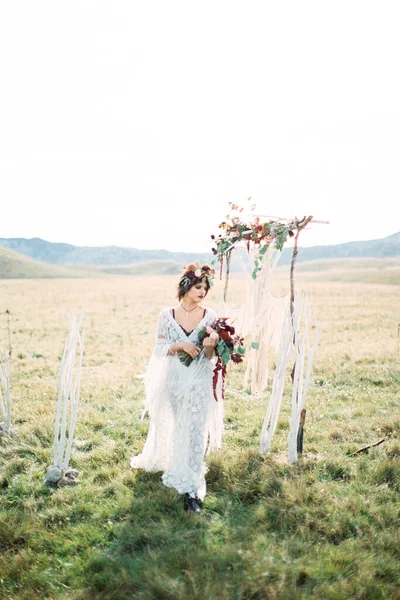 Noiva em uma grinalda com um buquê passa pelo arco de casamento — Fotografia de Stock