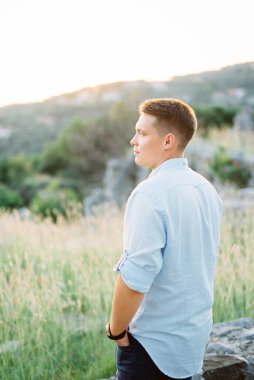 Elleri ceplerinde bir adam çimlerin üzerinde duruyor. Yan görünüm