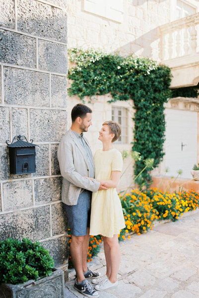 Man and woman are standing near a stone wall of a house near blooming flower beds Stock Image