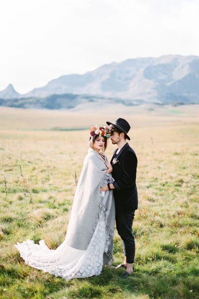 Noivo abraça noiva em uma planície em um campo verde — Fotografia de Stock