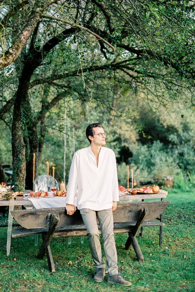 Чоловік стоїть спираючись на лавку за столом у зеленому саду — стокове фото