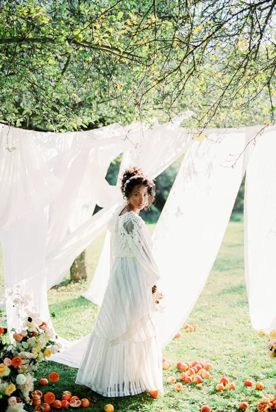 Uzun elbiseli kadın, bahçedeki yeşil çimlerin üzerindeki beyaz perdelerin yanında duruyor. — Stok fotoğraf