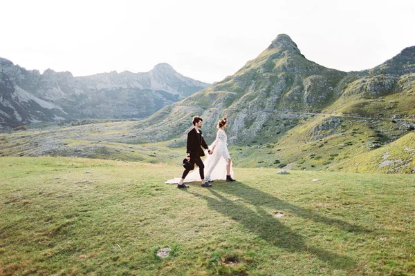 Noiva e noivo caminham pelo vale contra o pano de fundo das montanhas — Fotografia de Stock