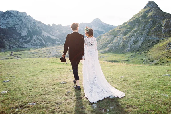 Bruid en bruidegom lopen hand in hand door het bergdal. Achteraanzicht — Stockfoto