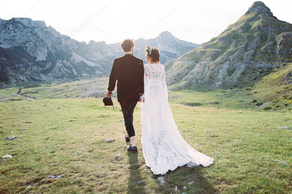 Bride and groom walk hand in hand through the mountain valley. Back view