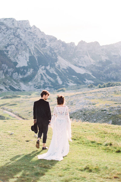 Bride and groom walk through the mountain valley. Back view Royalty Free Stock Images