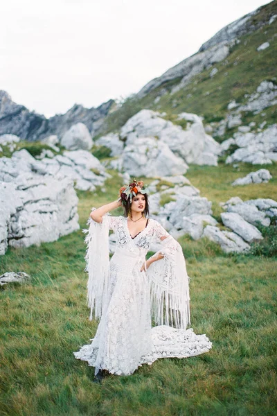 Bride in a wreath stands on green grass against the background of gray boulders Stock Image