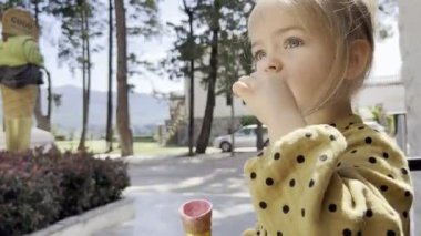 Little girl eats ice cream with a spoon in a waffle cone in a street cafe. High quality 4k footage