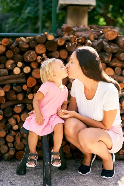 Mom kisses a little girl squatting next to her. High quality photo