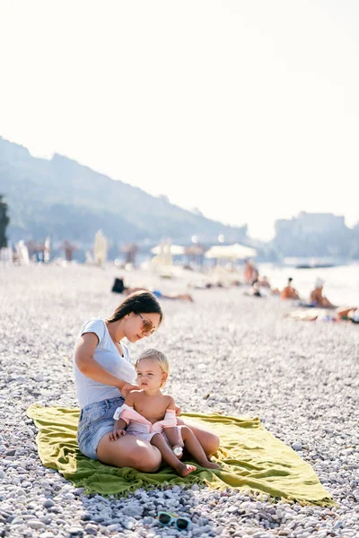 Mom applying sunscreen to little girl back while sitting on the beach. High quality photo