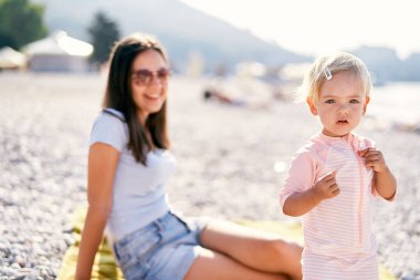Little girl stands on the beach near smiling mom. High quality photo