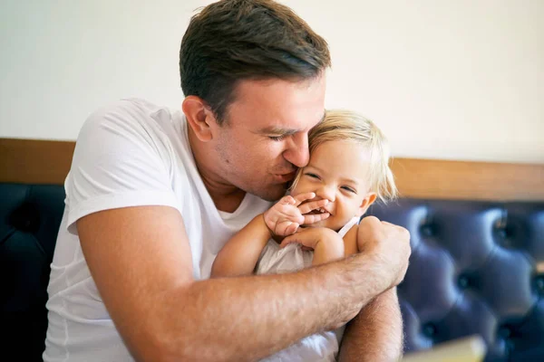 Smiling dad hugging and kissing little daughter lying on bed. High quality photo