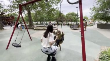Anne ve küçük kız parkta salıncakta sallanıyorlar. Yüksek kalite 4k görüntü