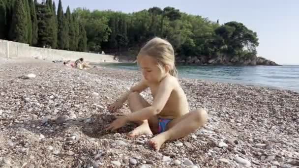 Gadis Kecil Menggali Lubang Dengan Tangannya Pantai Kerikil Dekat Air — Stok Video