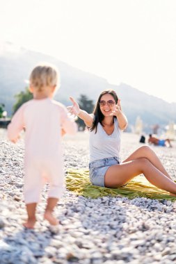 Little girl walks along the beach to her mother open arms. High quality photo