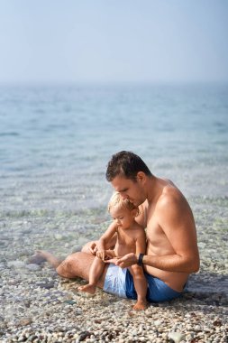 Babam ve küçük bir kız sığ sularda oturup deniz taşlarını ayırıyorlar. Yüksek kalite fotoğraf
