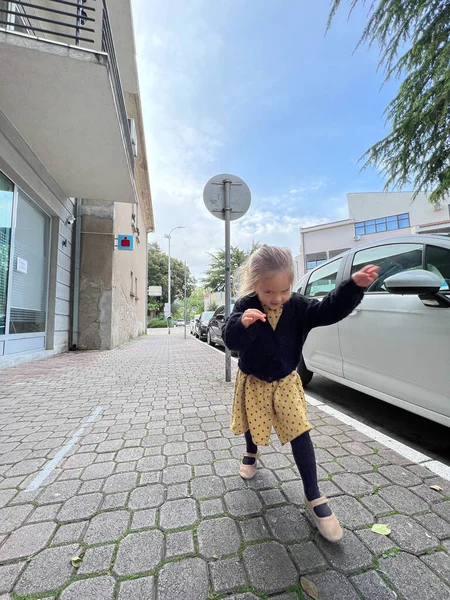 Little girl walks along the paving stones past a parked car. High quality photo