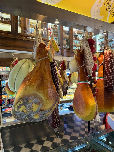 Huge hams and sausages hang from the ceiling near the shelves in the supermarket. High quality photo