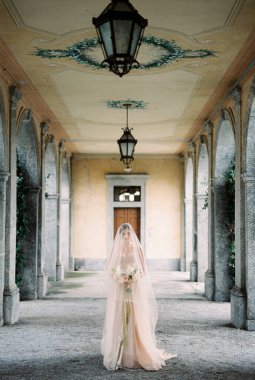 Peçeli gelinlik giymiş gelin, eski bir villanın terasında elinde buketle yürüyor. Yüksek kalite fotoğraf
