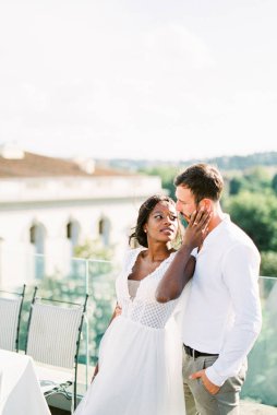 Bride hugs groom near the table on the roof of the building. High quality photo