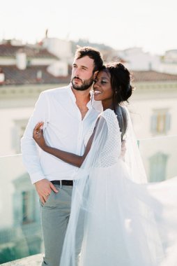 Bride and groom stand hugging on the roof of the building. High quality photo