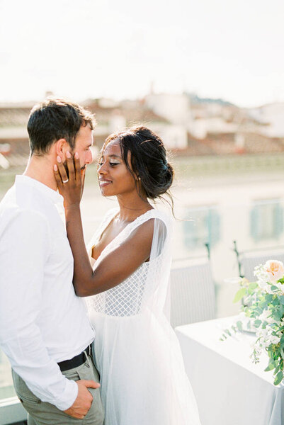 Smiling bride touches groom face with hands on terrace at home. High quality photo