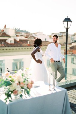 Bride stands next to groom near the table on the roof of the building. High quality photo