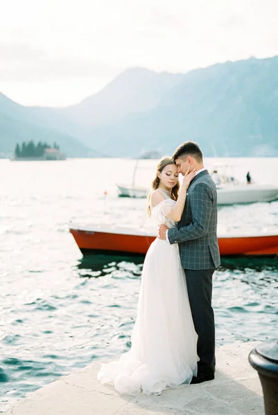 Groom Hugs Bride Pier Backdrop Boats Mountains High Quality Photo — стоковое фото