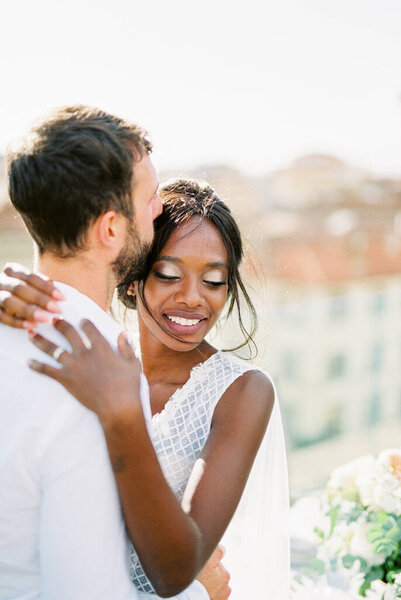 Groom hugs bride standing on the roof terrace. High quality photo