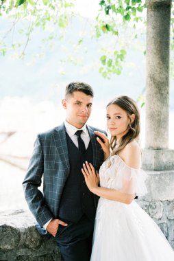 Bride and groom stand in a stone gazebo near the column. High quality photo