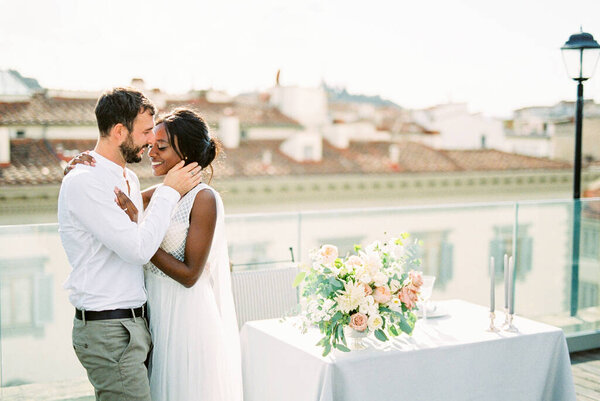 Groom hugs bride standing on the roof terrace near the table. High quality photo