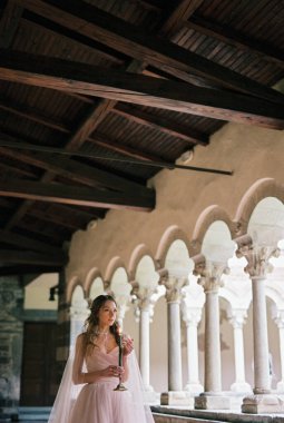 Bride with a lit candle walks along the terrace against the backdrop of columns. High quality photo