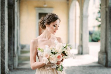 Bride with a bouquet of flowers in her hands on the terrace with arches. High quality photo