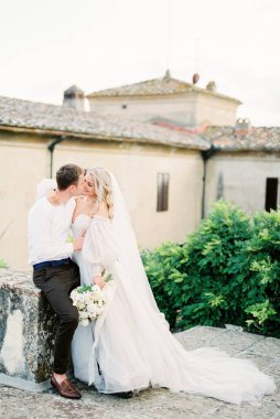 Bride and groom hug on the terrace of an old villa near the green bushes. High quality photo