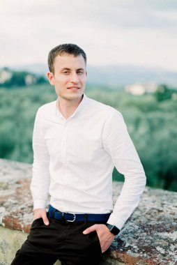 Man in a white shirt sits near a stone fence in the garden. High quality photo