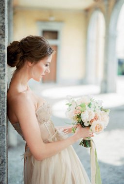 Bride with a bouquet in her hands leaned against the column. Side view. High quality photo