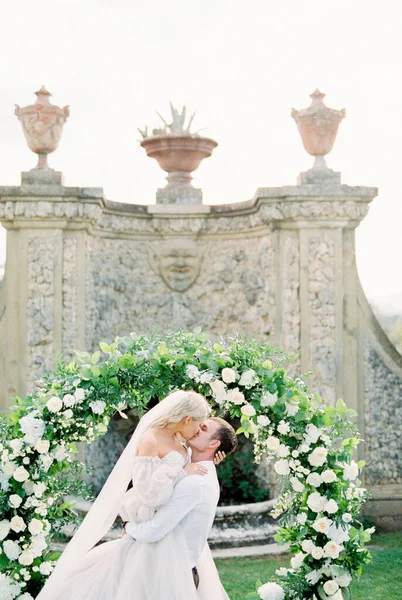 Groom Holds Kisses Bride His Arms Wedding Arch Garden High — Stockfoto
