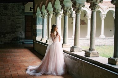 Bride stands with her arms folded across her chest on the terrace of an old villa. Lake Como, Italy. High quality photo