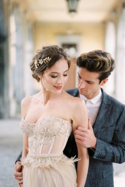 Groom hugs bride in a beige dress from behind. Portrait. High quality photo