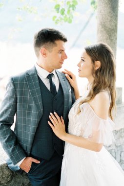 Bride put her hand on the shoulder of the groom standing in a stone gazebo. High quality photo