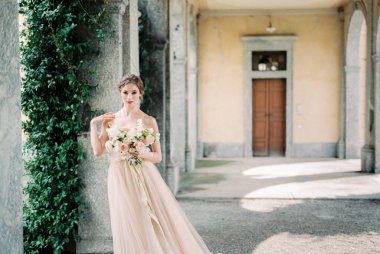 Bride stands on the terrace of an old villa near the column. High quality photo