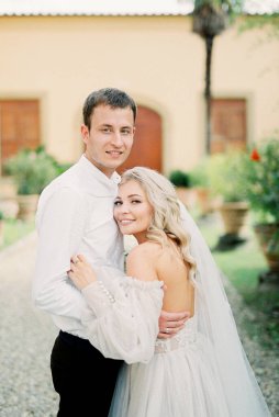 Bride and groom stand hugging in the garden near the villa. High quality photo