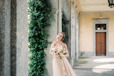 Bride with a bouquet stands on the terrace of an old villa near the column. High quality photo