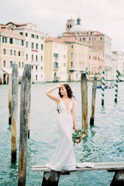 Bride with a bouquet stands on a wooden bridge against the backdrop of old houses in Venice. High quality photo