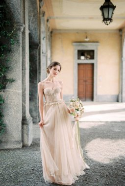 Bride with a bouquet stands on a terrace with arches of an old villa. High quality photo