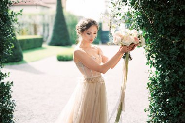 Bride holds a bouquet in her hands near a green bush. High quality photo