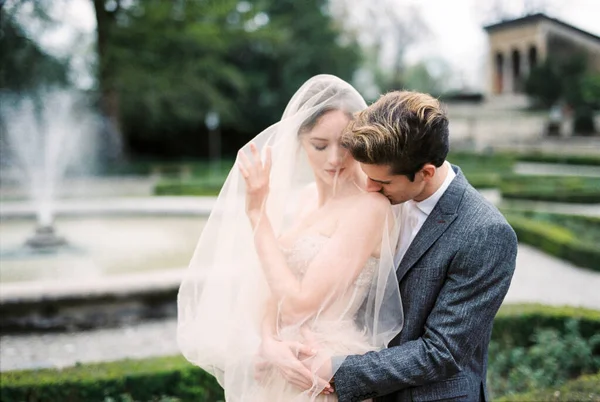 Groom Hugs Bride Veil Kisses Her Shoulder Fountain High Quality — Zdjęcie stockowe