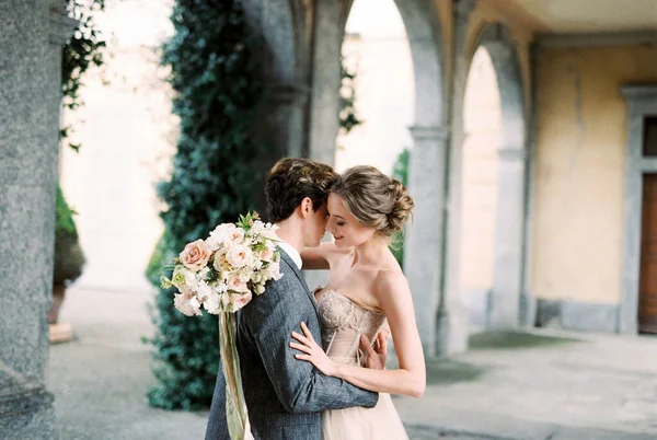 Groom Hugs Bride Bouquet Flowers Arches Old Villa Como Italy — Stock fotografie