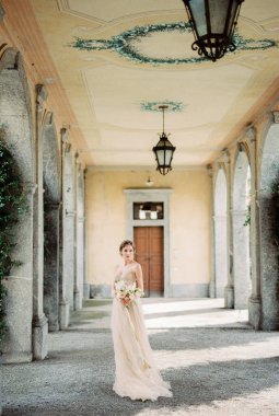 Bride in a beige dress stands on the terrace of an old villa. High quality photo